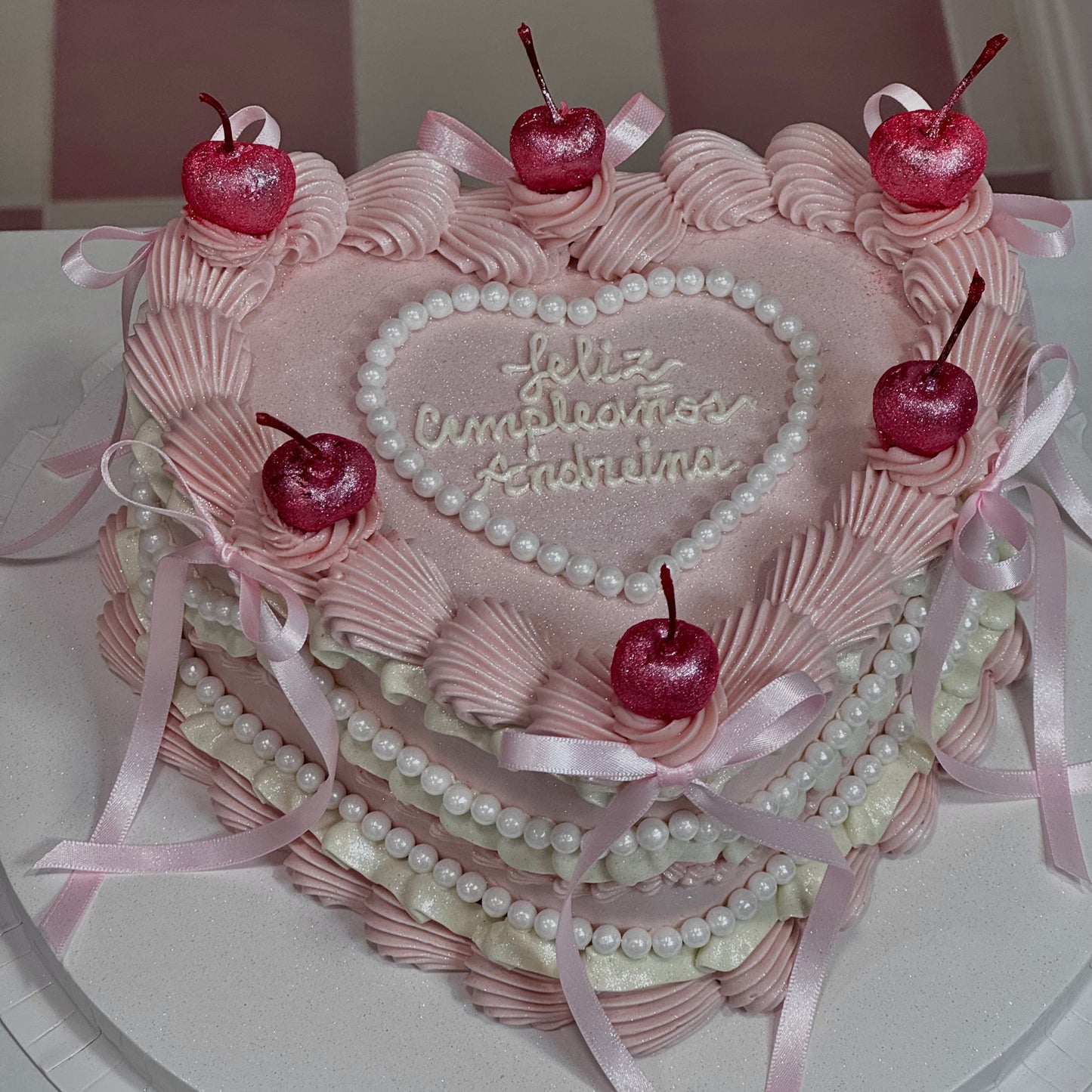 Tarta vintage rosa con cerezas brillantes, perlas blancas y crema decorativa en capas, estilo personalizado.