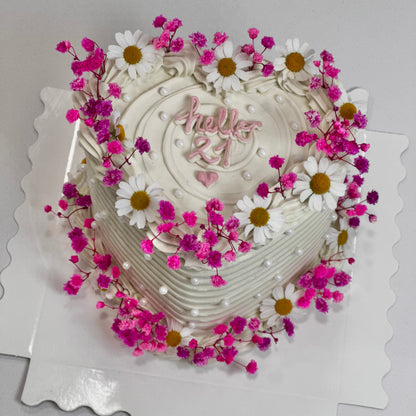 Tarta corazón decorada con flores secas en rosa y margaritas blancas, mensaje “Hello 21” en crema. Perfecta para celebrar los 21 con estilo artesanal.