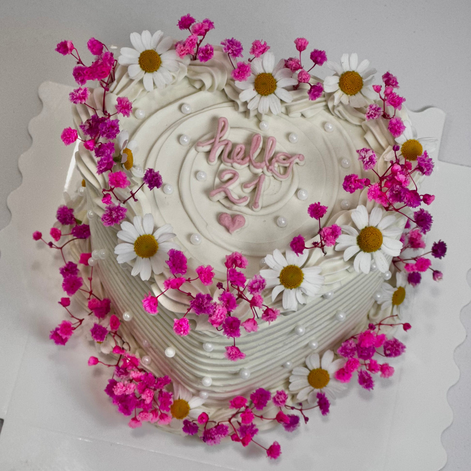 Tarta personalizada de cumpleaños con mensaje “Hello 21”, crema blanca y flores naturales secas. Diseño en forma de corazón, elegante y femenino.