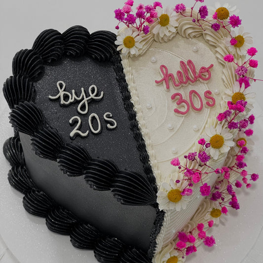 Tarta personalizada en forma de corazón con crema blanca y negra, flores naturales y mensaje “Bye 20s, Hello 30s”. Ideal para cumpleaños 30 originales.